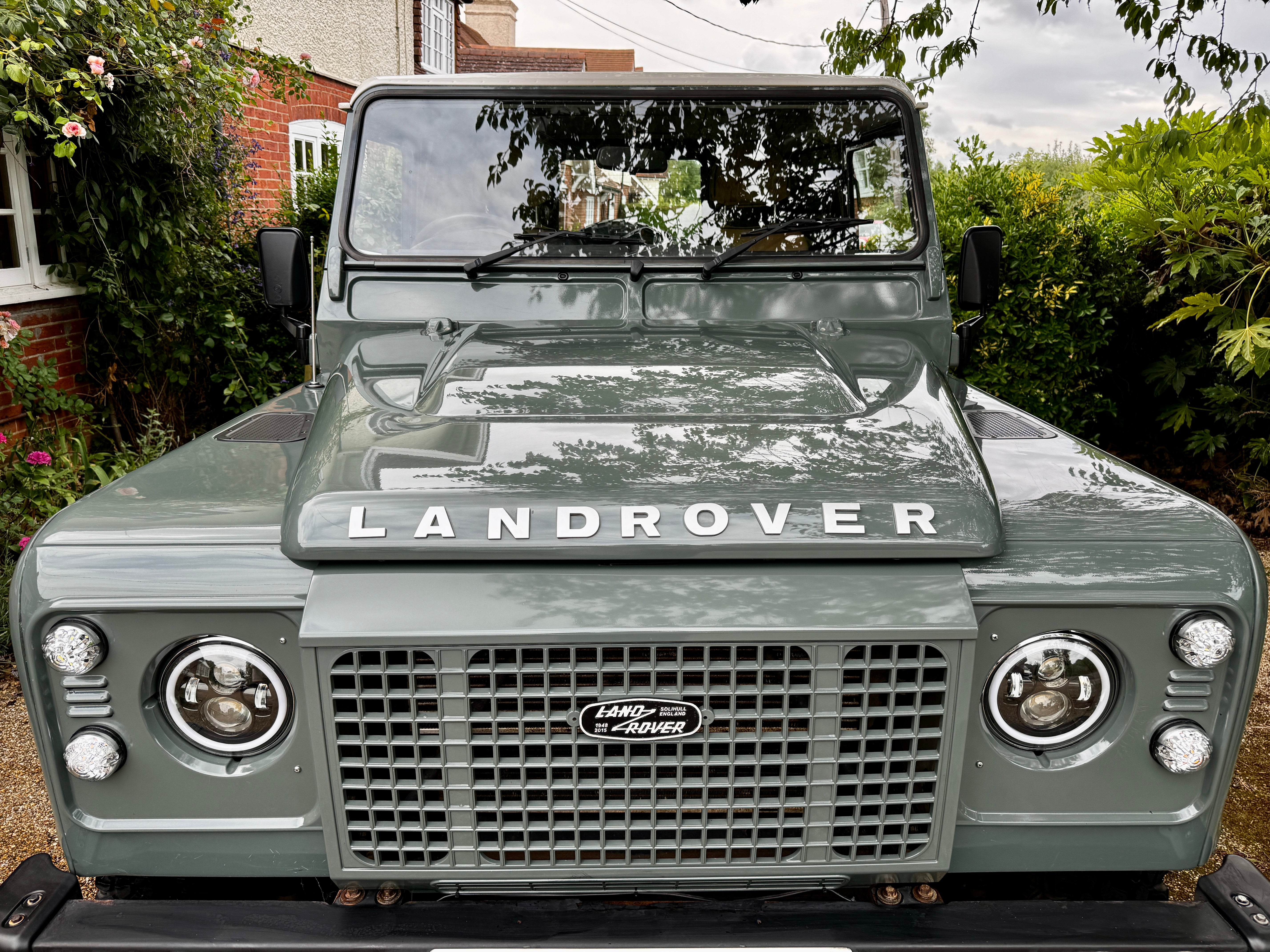 Front view of a Land Rover vehicle parked outdoors with greenery in the background.