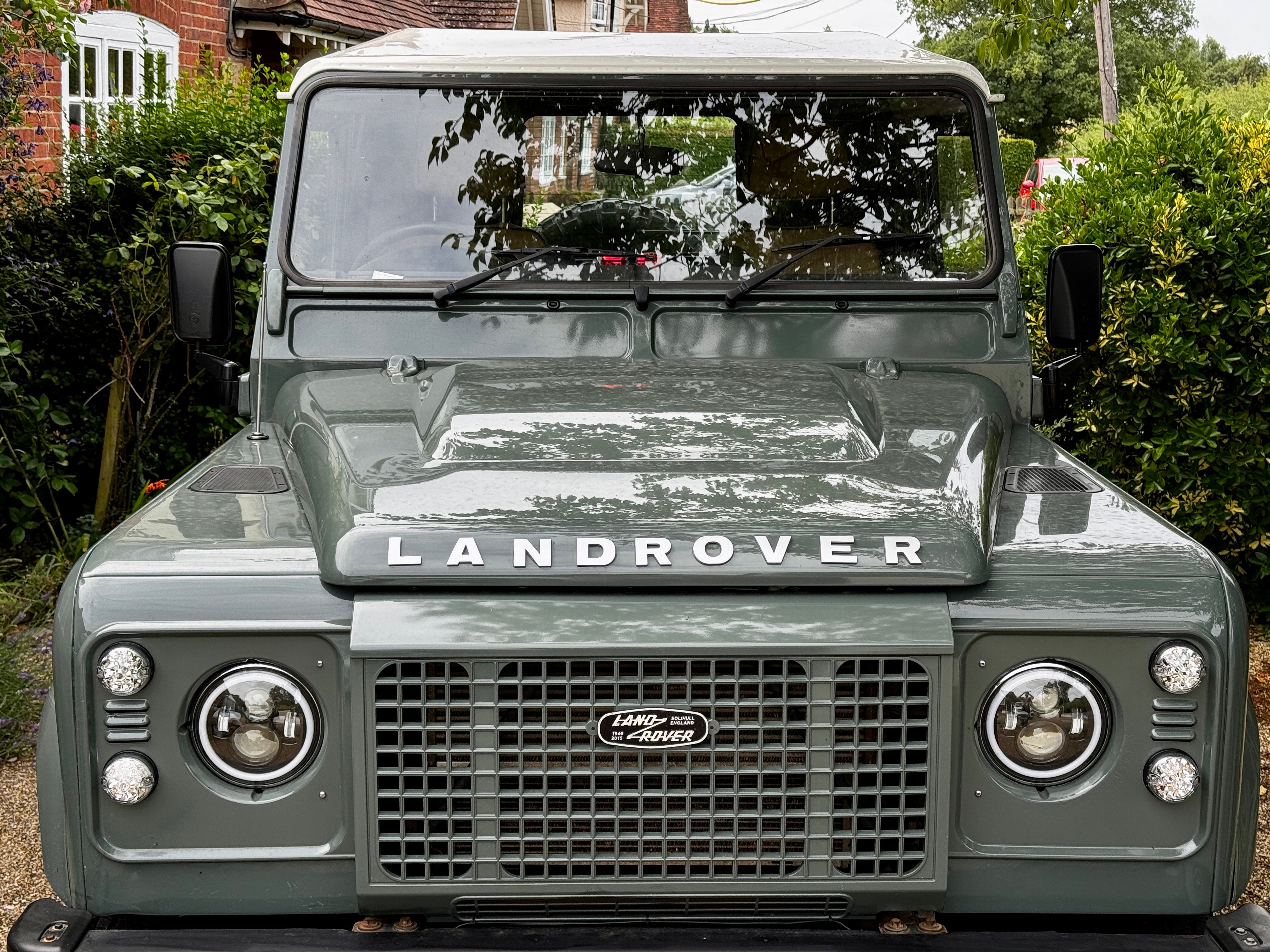 Front view of a Land Rover vehicle parked outdoors with greenery in the background.