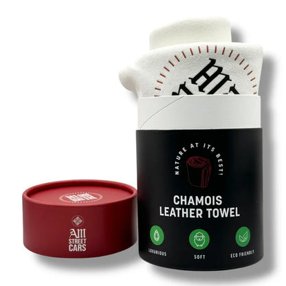 A premium chamois leather towel packaged in a black and white box with a red circular base. The packaging has white and red branding text and the towel appears soft and folded neatly.