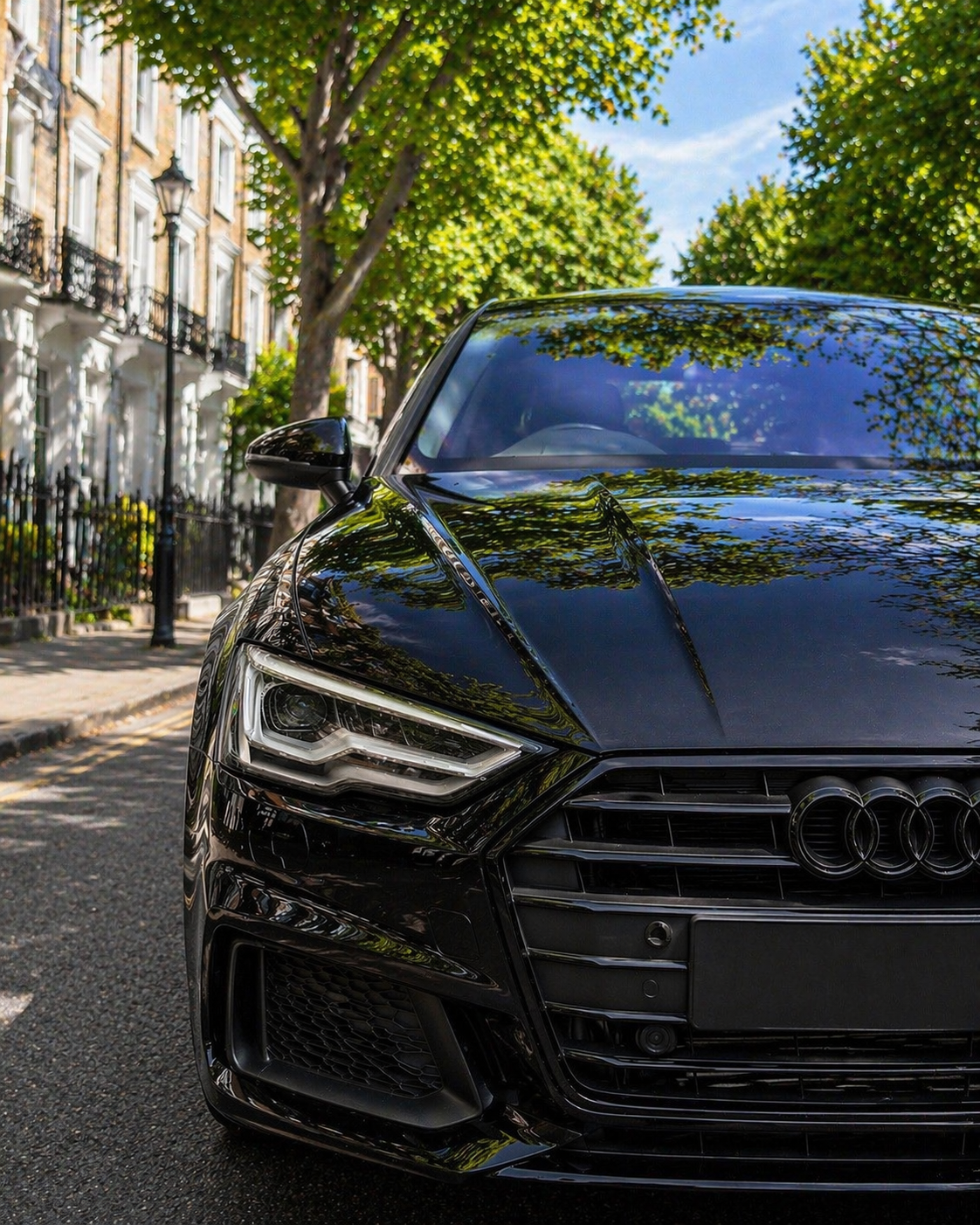 Black Audi car parked on a street with trees and buildings in the background